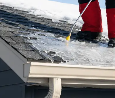 Ice dam removal technician using a steam wand to melt thick ice buildup on a residential roof in Spokane, WA